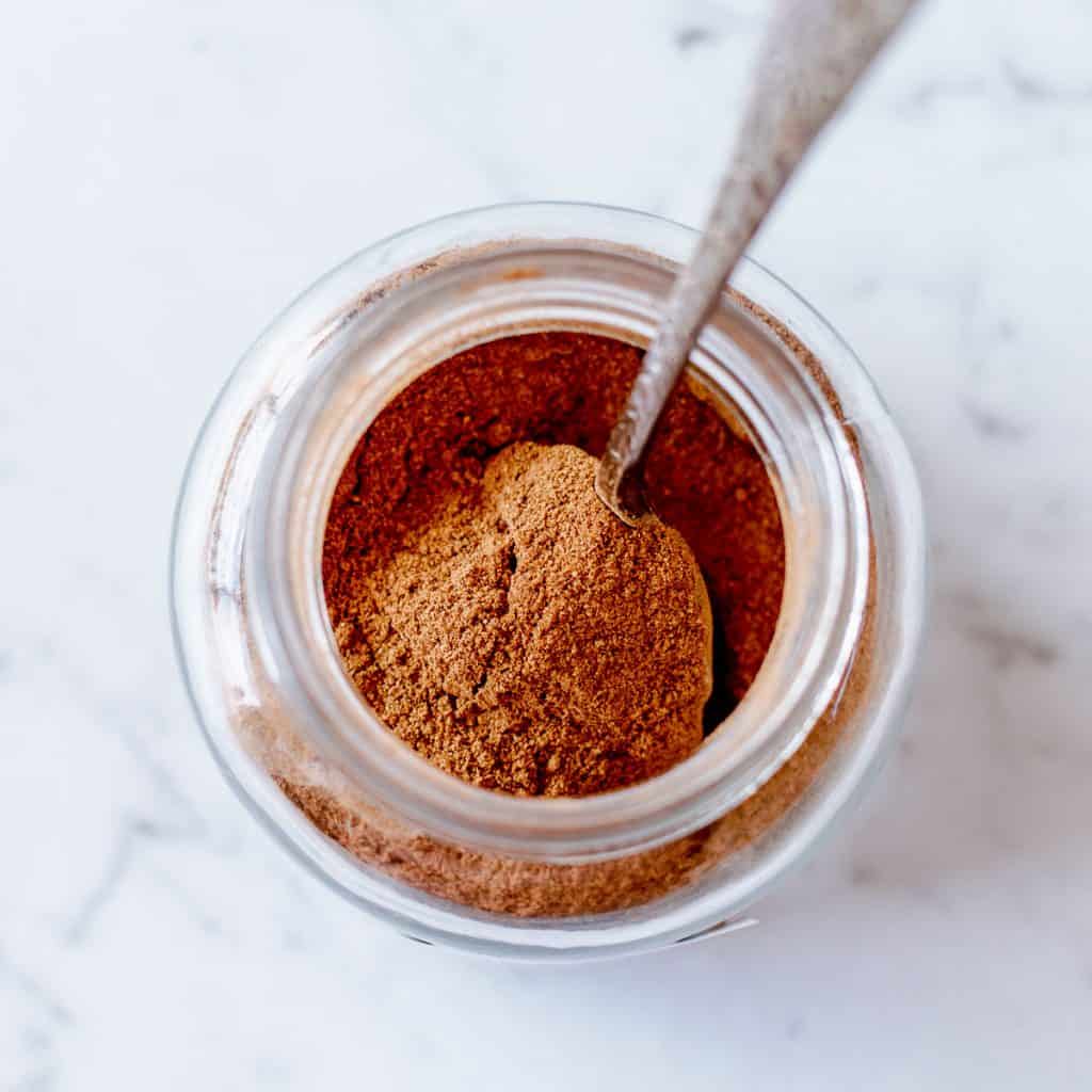 Overhead image of pumpkin spice mix in a glass jar sitting on a marble background.
