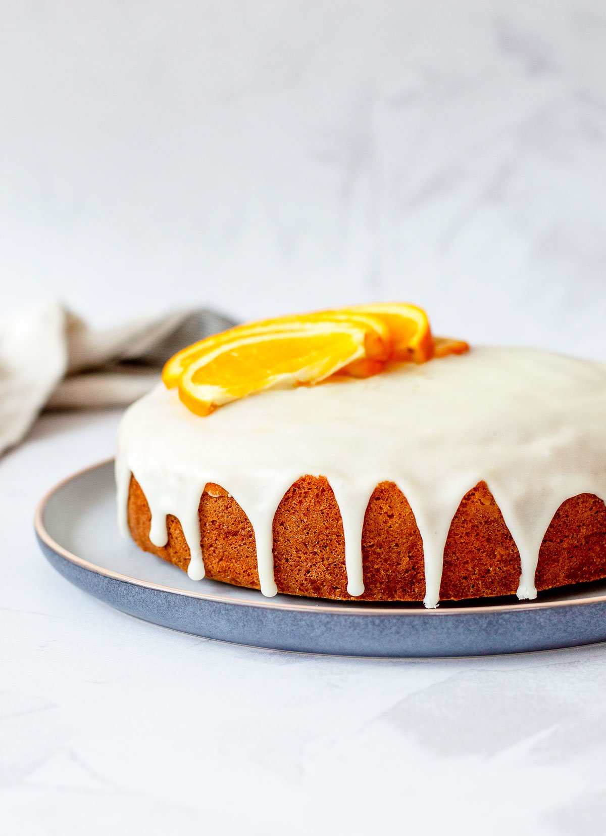 Moist orange cake topped with glossy orange glaze and garnished with fresh orange slices on a blue plate.