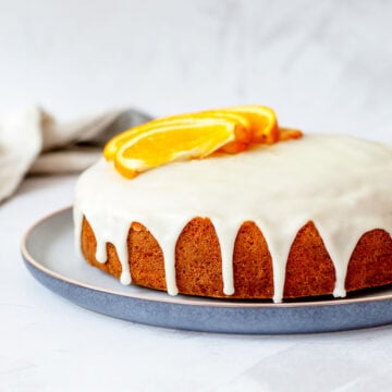 Easy orange cake recipe with icing, topped with fresh orange slices and served on a blue plate.